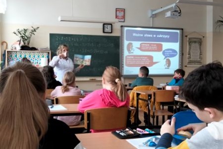 na środku klasy stoi pielęgniarka pokazuje uczniom książkę