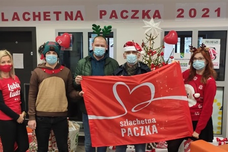pięć osób w maseczkach trzyma czerwony baner z napisałem szlachetna paczka