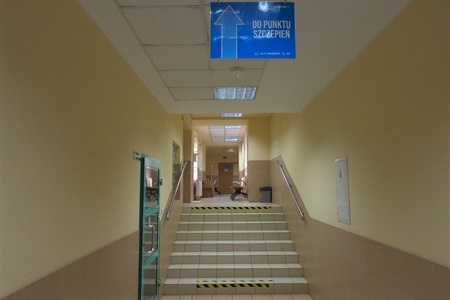 długi korytarz z kilkoma schodami oraz tabliczką wiszącą pod sufitem, na tabliczce napis do punktu szczepień