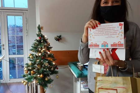 kobieta prezentuje kartkę świąteczną, trzyma papierowy torbę prezentową na tle choinki