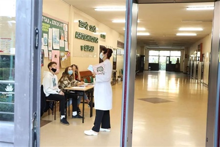 korytarz szklony, pielęgniarka w białym fartuchu rozmawia z uczniami siedzącymi na krzesłach